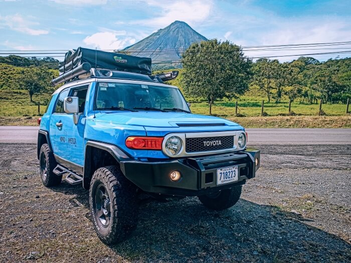 a large blue 4x4 Toyota with a backdrop of Arenal Volcano  