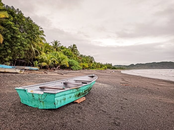 a turquoise fishermen boat on the grey sand of Samara beach on a cloudy day