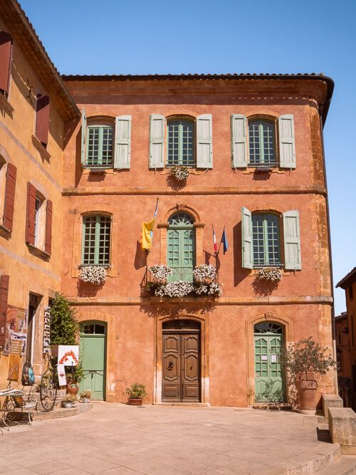 An ochre-colored house with blue window shutters in the village of Roussillon, a place that should be on every South of France road trip