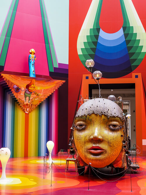 A colorful art installation consisting of a large yellow head surrounded by brightly painted walls and floor at Pinacoteca museum in Sao Paulo.