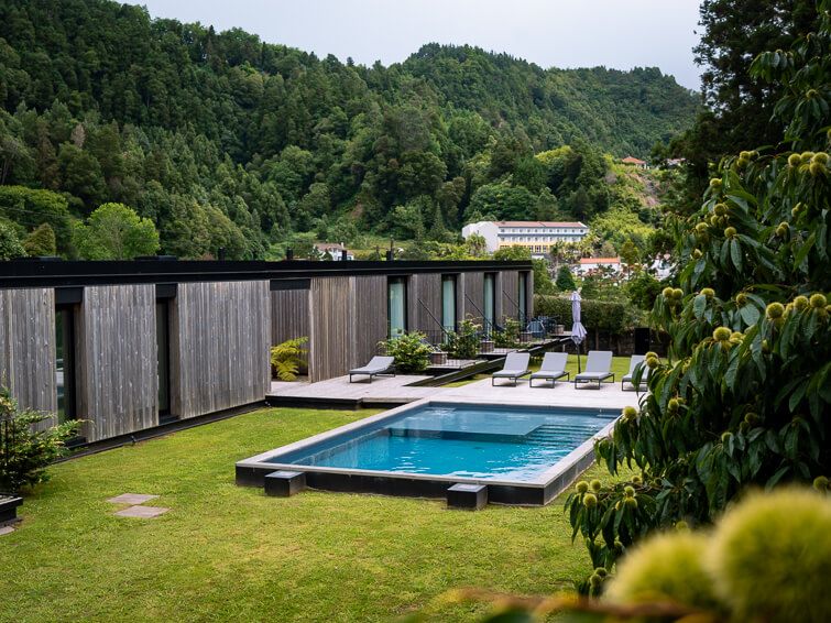 A swimming pool and sun loungers in the garden of Landescape Furnas hotel and mountains covered with forest in the background.