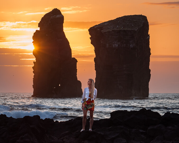 Me standing in front of two giant sea stacks at Mosteiros Beach during sunset, a must-see spot on this Azores itinerary.