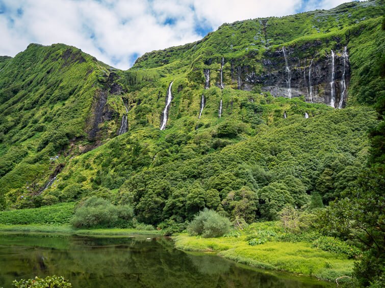 A row of waterfalls cascading down a steep mountainside covered with lush green vegetation