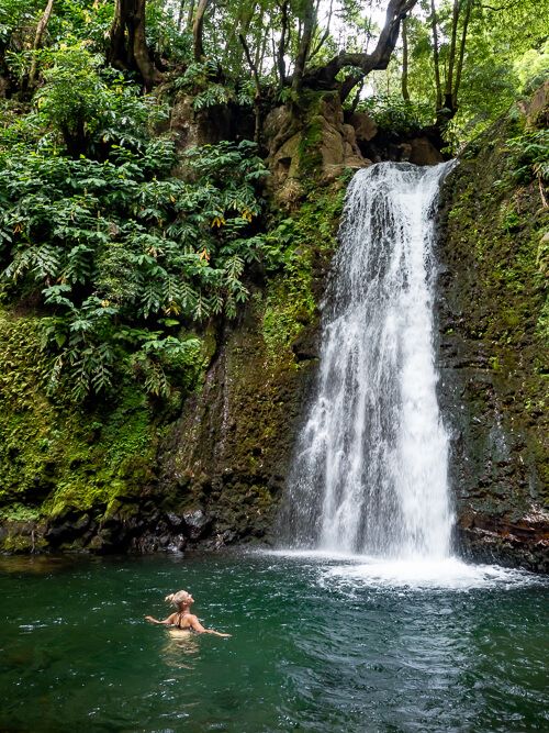 Me swimming in the pool of Salto do Prego waterfall surrounded by lush greenery and rocks covered with moss.