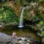 Me and my husband standing in front of the plunge pool of Cascata da Gruta waterfall surrounded by lush plants