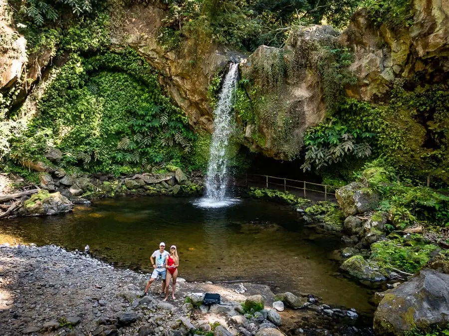 Me and my husband standing in front of the plunge pool of Cascata da Gruta waterfall surrounded by lush plants