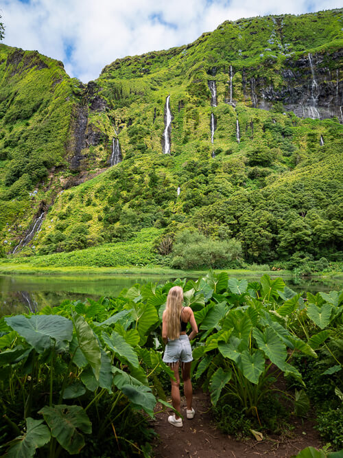 Me standing amidst abundant green vegetation in front of Cascata da Ribeira do Ferreiro waterfalls