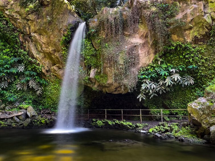 Cascata da Gruta waterfall plunging down an orange cliff into a natural pool below it.