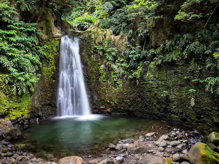 The waterfall of Salto do Prego cascading down green mossy rocks into a small pool, one of the most beautiful waterfalls in the Azores.