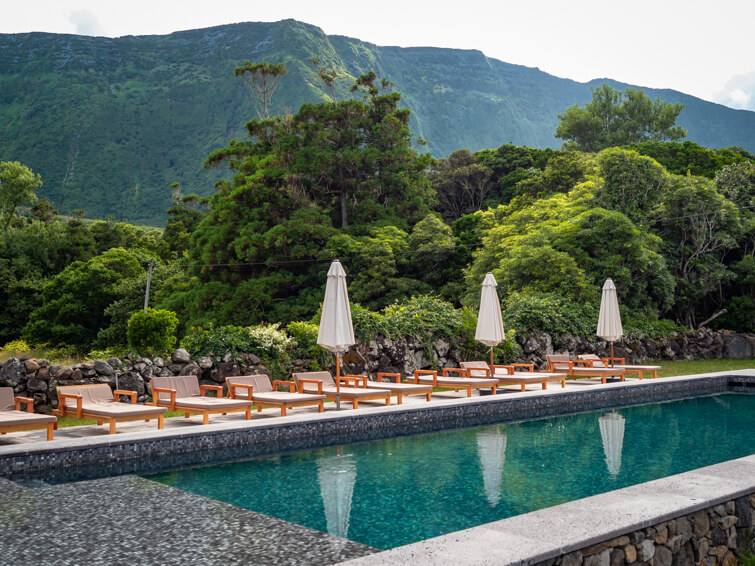 A swimming pool surrounded by sunbeds and parasols with towering green mountains in the background at Aldeia da Cuada hotel.