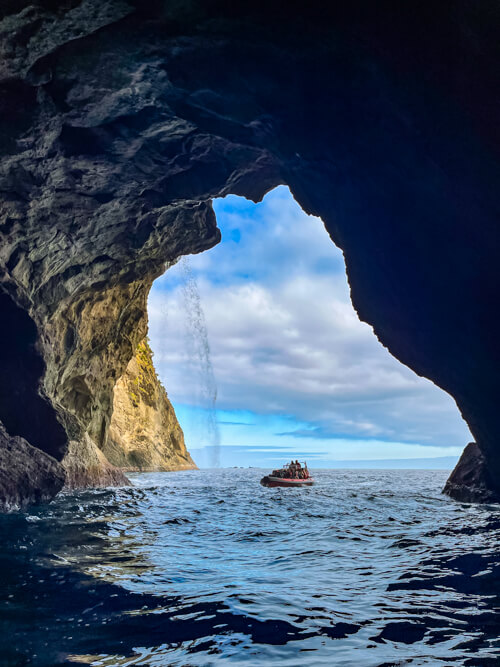 A boat stopping at the mouth of a large sea cave during a boat tour from Flores to Corvo.