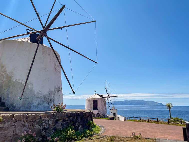 Two old whitewashed windmills on the coast of Corvo Island on a sunny day with blue skies.