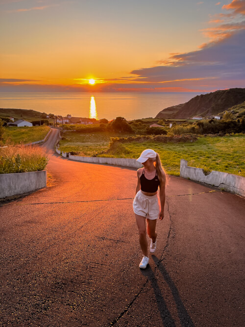 Me walking on the road in Fajãzinha village with a vibrant orange sunset in the background.