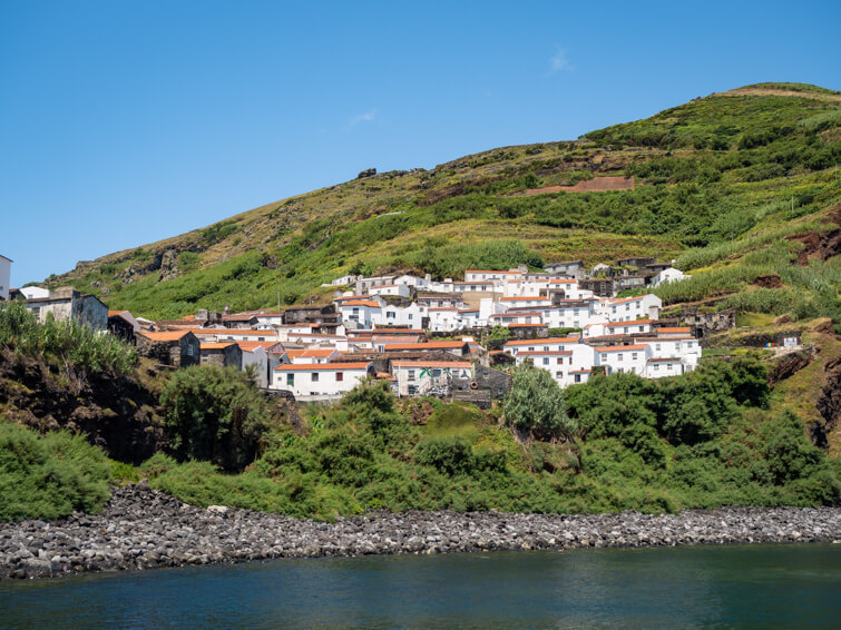 White buildings with terracotta-colored roofs in Vila do Corvo surrounded by green vegetation and fields.